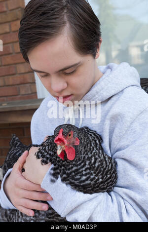 Teenage boy with autism and Down's Syndrome holding a barred rock hen in his arms outside Stock Photo