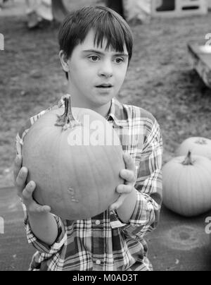 Teenage boy with Autism and Down's Syndrome holding a pumpkin, in black and white Stock Photo