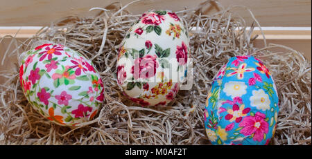 Three multi colored Easter eggs in straw laying in a wooden box Stock Photo