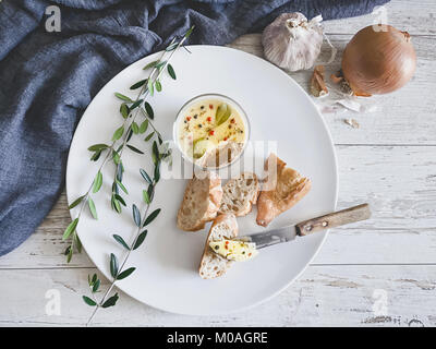 Chicken liver pate covered with melted butter and decorated with bay leaves and black and red pepper on white plate. Rustic wooden background. Top vie Stock Photo