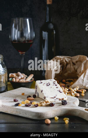Wensleydale cheese with cranberries, red wine, honey, nuts, raisins on wooden cutting board. Black concrete background. Selective focus. Stock Photo