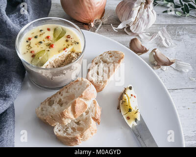 Fresh homemade chicken liver pate covered with melted butter and decorated with bay leaves and black and red pepper on white plate. Rustic wooden back Stock Photo