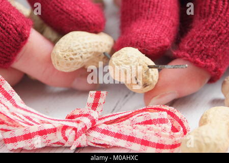 Creating a speedy, winter heart-shaped bird feeder from monkey nuts (step by step guide). Step1/3:Thread monkey nuts on craft wire fashioned as heart Stock Photo