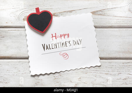 Valentine's card. Red clothespin as heart and sheet with wishes on wooden board. Copy space. Top view. Stock Photo
