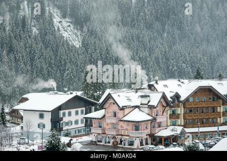 Pink, highly decorated hotel in Campitello with smoke from the chimneys and the tree-covered mountain with snow behind. Stock Photo