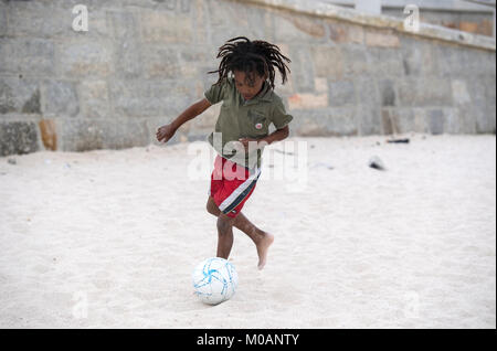 Young boy playing football on a sandy beach in Cape Town, South Africa Stock Photo