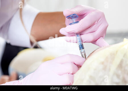 Close-up Young woman doctor cosmetician in white lab coat and sterile gloves makes Botox injection with syringe Stock Photo