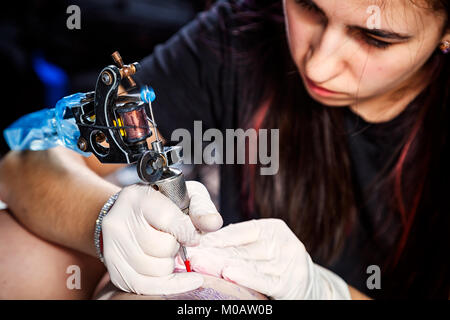 Close up hands with machine doing bird tattoo on woman's femur Stock Photo