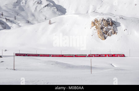 Famous Bernina red train walking through snow landscape between Italy and Suisse. Stock Photo