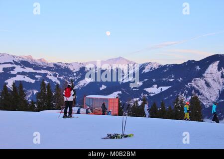 Skiers and mountain scenery with nearly full moon on the Areit cable car station (1400 m), in winter. Zell am See, Austria, Europe. Stock Photo