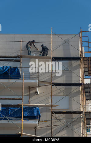 builders up scaffolding on the side of a block of flats Stock Photo