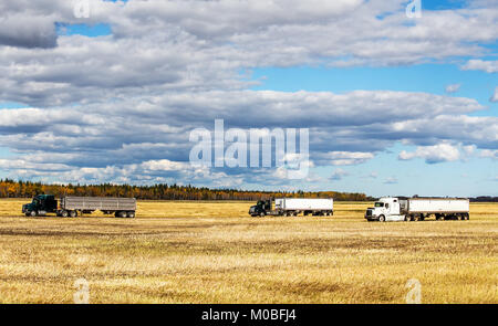 Three heavy transport truck and trailer parked in a golden harvested field under a cloudy and sunny countryside autumn landscape Stock Photo