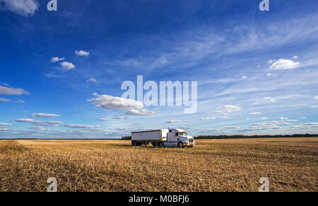 Heavy transport truck and trailer parked in a golden harvested field under a cloudy and sunny countryside autumn landscape Stock Photo
