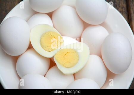 Numerous white hard boiled eggs in white bowl with two halves with yokes on top Stock Photo