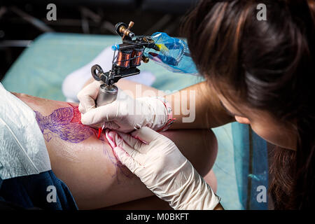 A close-up of the process of creating a bird tattoo by a female tattoo master on a hip under sterile conditions Stock Photo