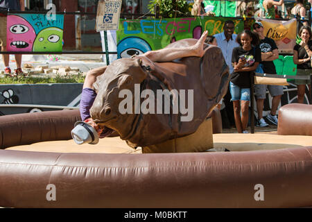 Atlanta, GA, USA - September 23, 2017:  A young man desperately tries to stay on a mechanical bull as he starts to fall, at the East Atlanta Strut, a  Stock Photo