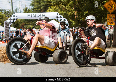 Atlanta, GA, USA - September 23, 2017:  Men race each other on adult big wheels in a friendly competition at the East Atlanta Strut festival. Stock Photo