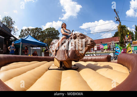 Atlanta, GA, USA - September 23, 2017:  A young woman tries to stay upright as she rides a mechanical bull at the East Atlanta Strut festival. Stock Photo