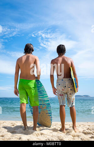 Young Brazilian men stand with skimboards on the shore of Ipanema Beach in Rio de Janeiro, Brazil Stock Photo