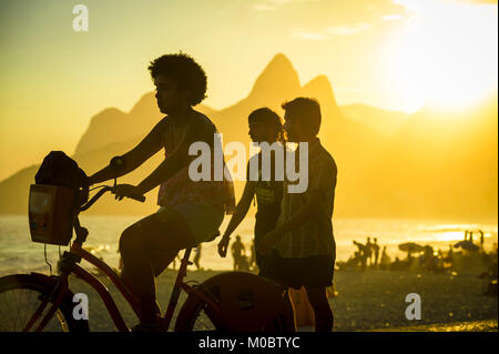 RIO DE JANEIRO - MARCH 20, 2017: Visitors pass along Ipanema Beach to Arpoador, a popular spot to take in the sunset against Two Brothers Mountain. Stock Photo