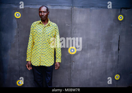 BURKINA FASO, Ouagadougou, man in yellow shirt in front of steel gate with yellow dots Stock Photo