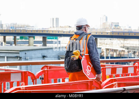 Back view of a construction worker with a stop waning sign in a building site in Canary Wharf, London Stock Photo