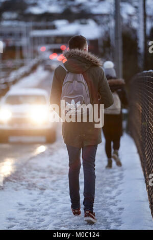 young man carrying backpack walking along footpath on street covered in snow in newtownabbey northern ireland Stock Photo