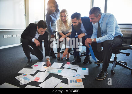 Diverse group of corporate professionals strategizing together with paperwork laid out on the floor while working in a modern office Stock Photo
