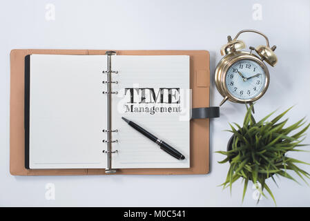 golden bell clock, green plant and blank notebook with TIME MANAGEMENT word on white flat lay. time management concept Stock Photo