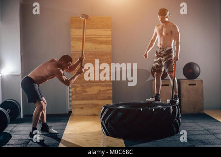 Sledgehammer Tire Hits men workout at gym with hammer and tractor tire Stock Photo