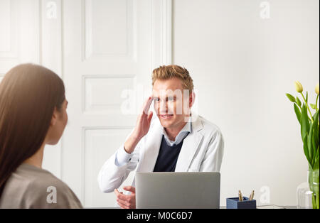 Beautician sitting and touching his face while consulting young woman and sitting at laptop. Stock Photo