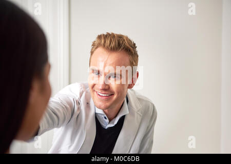 Smiling handsome cosmetologist man in salon consulting woman and touching her face. Stock Photo