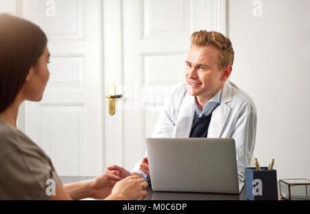 Professional cosmetologist man sitting at laptop in office and consulting young female client. Stock Photo