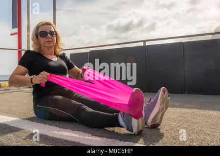 Model Released: Mature woman (70-75) stretching with a stretch cord at open air public gym in Ipanema Beach, Rio de Janeiro, Brazil Stock Photo