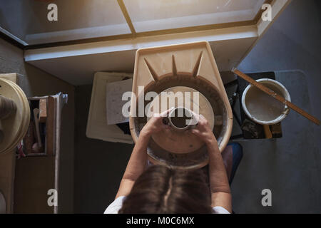 Female artisan using her hands to shape a wet piece of clay turning on a wheel while working in her pottery studio Stock Photo