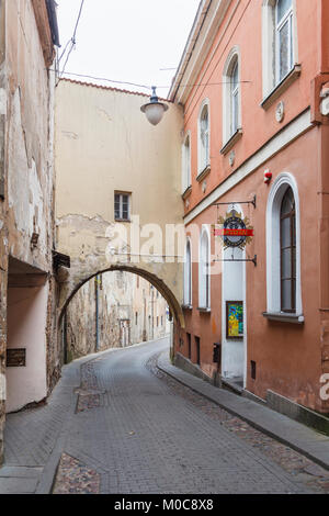 The narrow Sv Kazimiero Gatve with old dilapidated arch built over the road in the Old Town of Vilnius, capital city of Lithuania, and bar sign Stock Photo