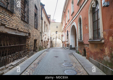 The narrow Sv Kazimiero Gatve with old dilapidated arch built over the road in the Old Town of Vilnius, capital city of Lithuania, and bar sign Stock Photo