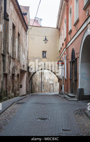 The narrow Sv Kazimiero Gatve with old dilapidated arch built over the road in the Old Town of Vilnius, capital city of Lithuania, and bar sign Stock Photo