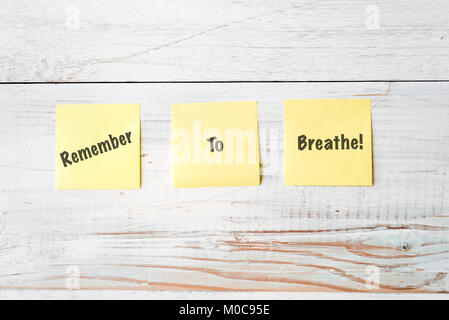 three yellow Post It notes with message Remember To Breathe! against weathered white wood background Stock Photo