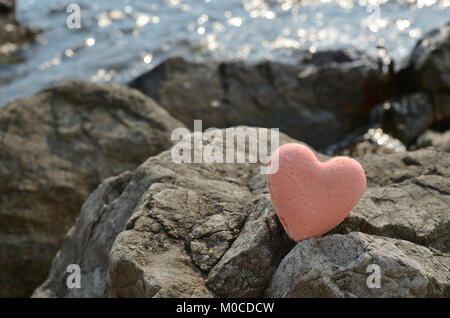 Pink bath salt figure in a heart shape on a sea rock with a sea water behind Stock Photo