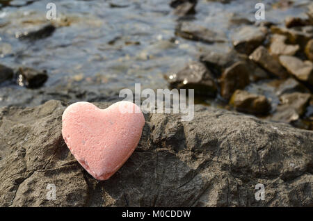 Pink bath salt figure in a heart shape on a sea rock Stock Photo