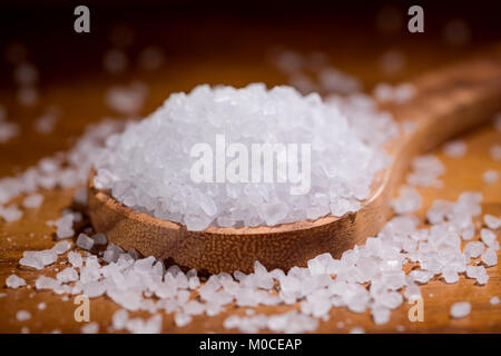 Sea salt crystals closeup in wooden spoon on a kitchen table. Stock Photo