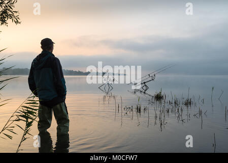Fishing adventures, carp fishing. Early morning with mist and fisherman with high rubber boots Stock Photo