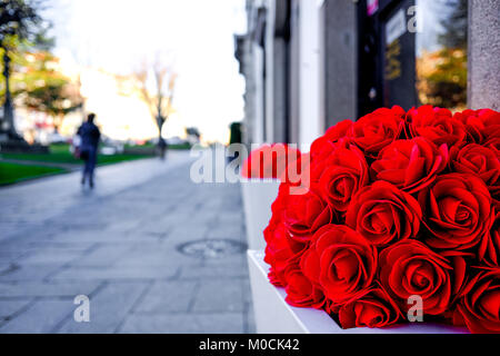 color, colorful, objects, houses, the contrasts of a beautiful, but artificial bouquet of red roses right on the the street in a gorgeous sunny day. Stock Photo
