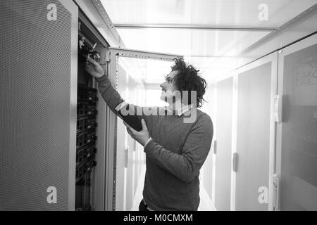 young IT technician using digital cable analyzer on server in large data center Stock Photo