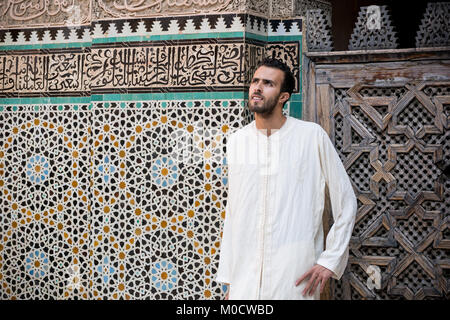 Arab man wearing traditional clothing, long white shirt in front of the wall with text from Koran Stock Photo