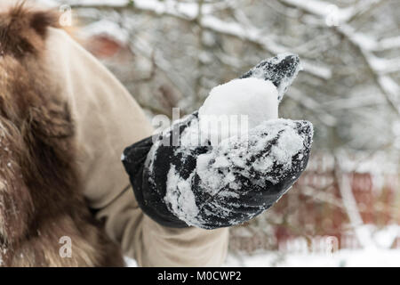 A hand wearing warm glove holding snowball, outdoor selective focus shot Stock Photo
