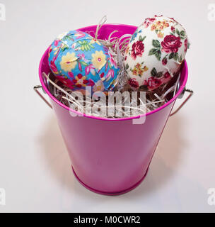 Two multi colored Easter eggs in a pink bucket which is filled with straw Stock Photo