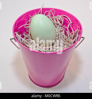 A single Easter egg in a pink bucket that is filled with straw Stock Photo