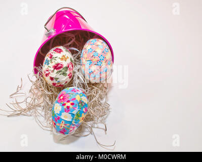 Easter eggs shown spilling out of a pink bucket along with straw on a white background Stock Photo
